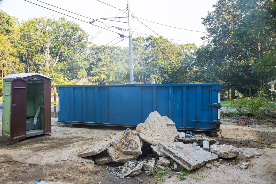 removal of debris construction waste building demolition with rock and concrete rubble on portable bio toilet cabins at the construction site with roll off dumpsters